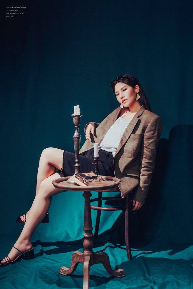 模特兒側身倚靠椅背，展示女西服背部與袖子的流暢結構